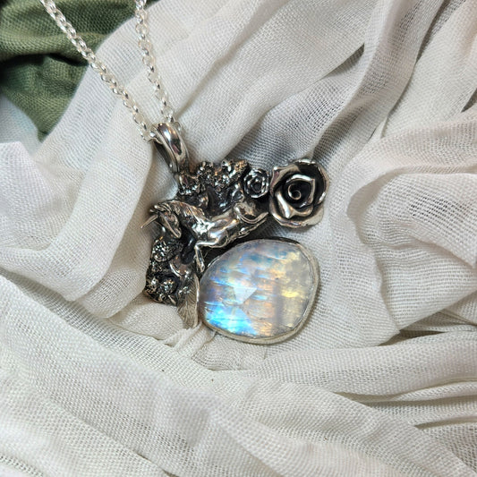 a large sterling silver necklace of a sculpted unicorn, roses, and various foiage, with a large vibrant rainbow moonstone dangling underneath